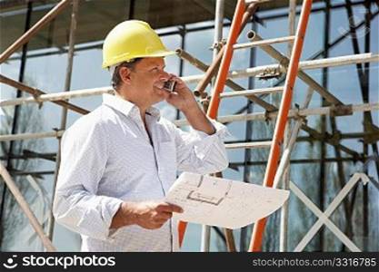 Architect With Plans Outside New Home Talking On Mobile Phone