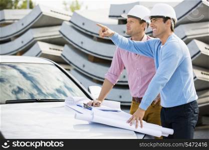 Architects with blueprints on car discussing at site