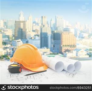 architectural blueprint with safety helmet and tools over modern business district with high building