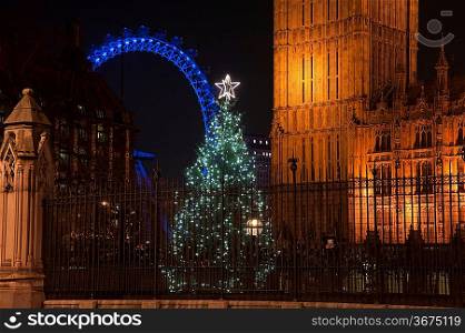 Architectural detail of Houses of Parliament in London England with Christmas tree in foreground and London Eye in background