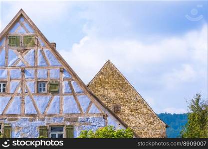 Architectural details from two medieval German houses , one with blue half timbered walls, small windows, wooden shutters and one with aged  stone wall and a single wooden window.