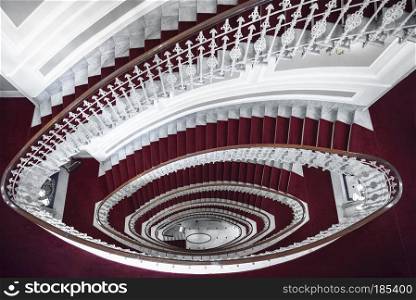 Architectural symmetry with elegant spiral stairways,  above view, made of white marble and covered with red carpet, in a hotel in Genoa, Italy.