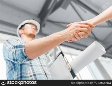 architecture and home renovation concept - builder with blueprint shaking partner hand