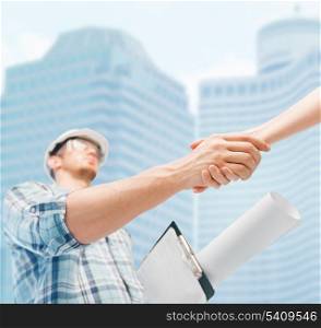 architecture and home renovation concept - builder with blueprint shaking partner hand