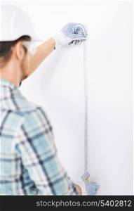 architecture and home renovation concept - male architect measuring wall with flexible ruler
