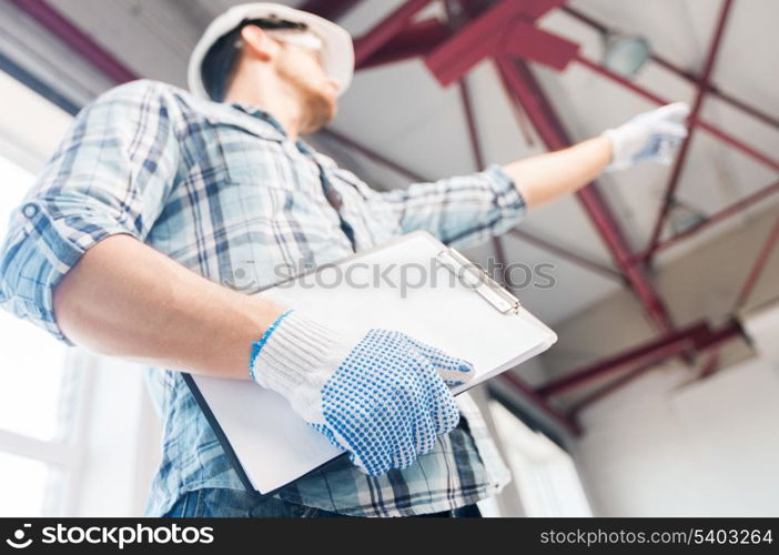 architecture and home renovation concept - man in helmet and gloves with blueprint in factory