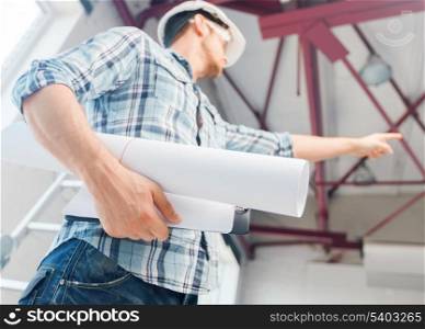 architecture and home renovation concept - man in helmet and gloves with blueprint showing direction