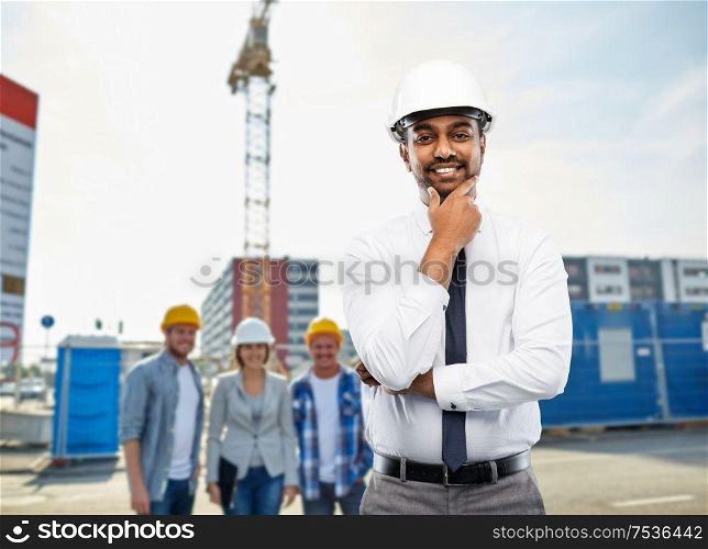 architecture, building business and people concept - smiling indian male architect in helmet over construction site background. indian architect in helmet over construction site