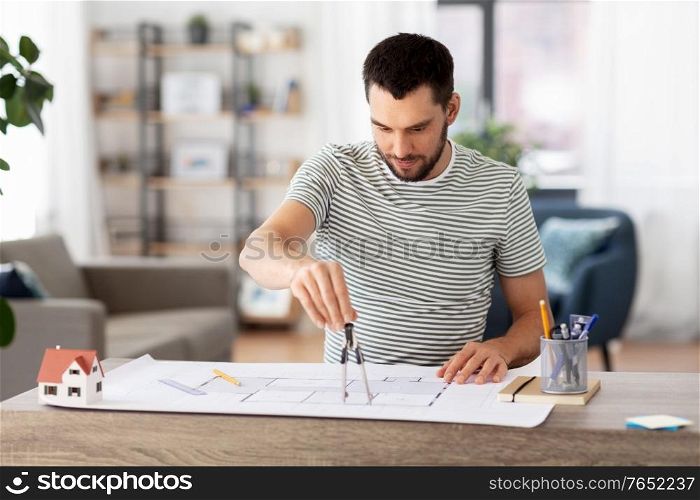 architecture, building, construction and real estate concept - male architect with compass measuring blueprint on table working at home office. architect with blueprint working at home office