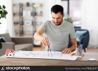 architecture, building, construction and real estate concept - male architect with compass measuring blueprint on table working at home office. architect with blueprint working at home office