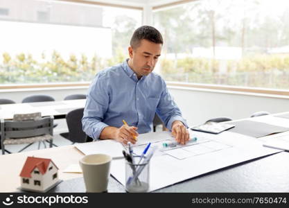 architecture, building, construction and real estate concept - middle-aged male architect with blueprint, ruler and living house model on table working at home office. architect with blueprint working at home office