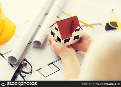 architecture, building, construction, real estate and people concept - close up of architect hands holding living house model above blueprint on table. close up of hands with house model above blueprint