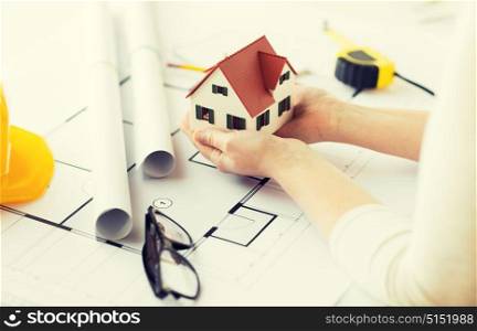 architecture, building, construction, real estate and people concept - close up of architect hands holding living house model above blueprint on table. close up of hands with house model above blueprint