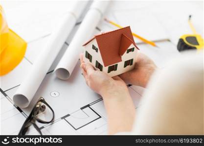 architecture, building, construction, real estate and people concept - close up of architect hands holding living house model above blueprint on table