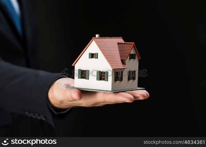 architecture, building, construction, real estate and property concept - close up of businessman or real estate agent hand holding house or home model over black background