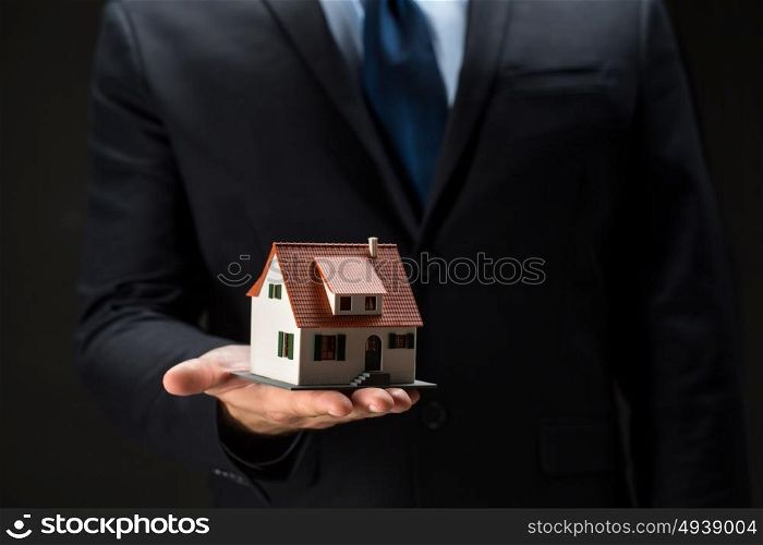 architecture, building, construction, real estate and property concept - close up of businessman or real estate agent holding house or home model on palm over black background. close up of businessman holding house model