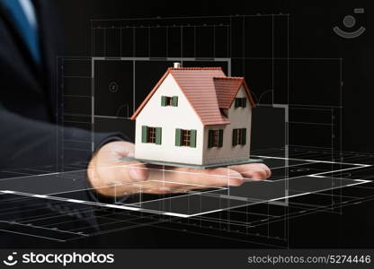 architecture, building, construction, real estate and property concept - close up of businessman or architect hand holding house model over black background. close up of businessman hand holding house model