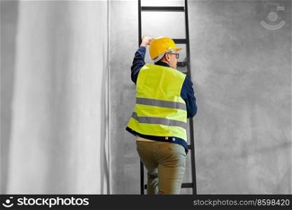 architecture, construction and building concept - male builder or worker in helmet and safety west climbing ladder or stairs. builder or worker in helmet climbing ladder