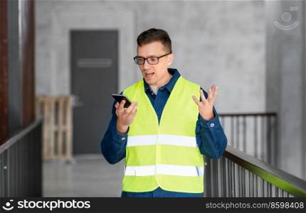 architecture, construction business and building concept - angry male architect in safety west calling on smartphone or using voice command recorder at office. male architect calling on smartphone at office
