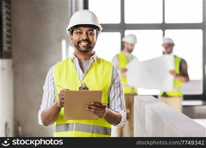 architecture, construction business and building concept - happy smiling male architect in helmet and safety west with clipboard working at office. male architect in helmet with clipboard at office