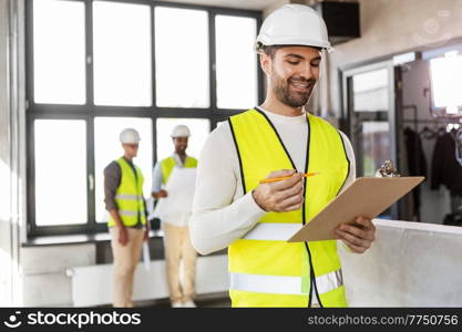 architecture, construction business and building concept - happy smiling male architect in helmet and safety west with clipboard working at office. male architect in helmet with clipboard at office