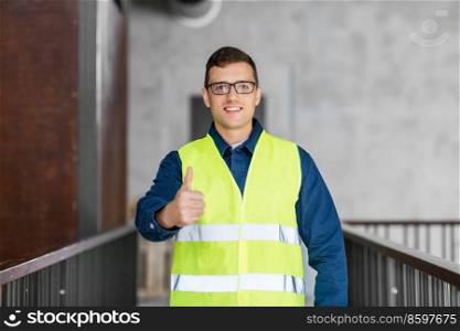 architecture, construction business and building concept - happy smiling male architect in safety west showing thumbs up gesture at office. male architect in safety west showing thumbs up