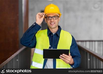 architecture, construction business and building concept - happy smiling male architect in helmet and safety west with tablet pc computer at office. architect in helmet and safety west with tablet pc
