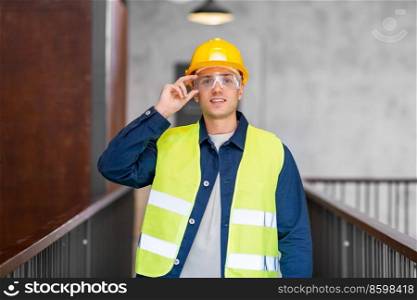 architecture, construction business and building concept - happy smiling male architect in helmet, goggles and safety west at office. male architect in helmet and goggles at office