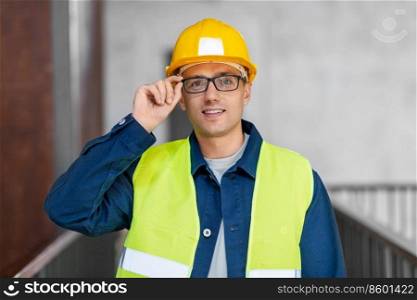 architecture, construction business and building concept - happy smiling male architect in helmet and safety west at office. male architect in helmet and safety west at office