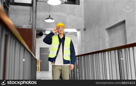 architecture, construction business and building concept - happy smiling male builder in helmet, goggles and safety west at office. male builder in helmet and goggles at office