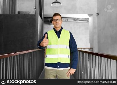 architecture, construction business and building concept - happy smiling male worker in safety west showing thumbs up gesture at office. male worker in safety west showing thumbs up