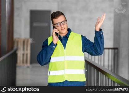 architecture, construction business and building concept - male architect in safety west calling on smartphone at office. male architect calling on smartphone at office