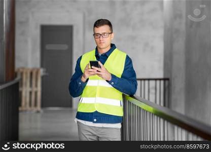 architecture, construction business and building concept - male architect in safety west with smartphone at office. male architect with smartphone at office