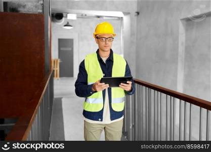 architecture, construction business and building concept - male supervisor in helmet and safety west with tablet pc computer at office. worker in helmet and safety west with tablet pc