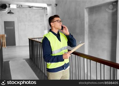 architecture, construction business and building concept - male supervisor in safety west with clipboard calling on smartphone at office. male supervisor with clipboard calling on phone