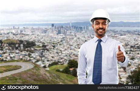 architecture, construction business and building - smiling indian architect or businessman in helmet showing thumbs up over san francisco city background. architect or businessman in helmet shows thumbs up