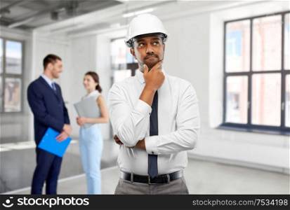 architecture, construction business and occupation concept - thinking indian male architect in helmet over people in empty office room background. indian male architect in helmet at office room