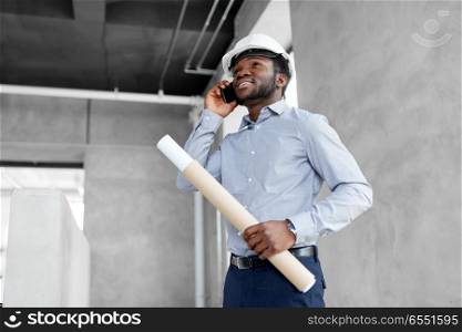 architecture, construction business and people concept - african american architect in helmet with blueprint calling on smartphone. architect with blueprint calling on smartphone. architect with blueprint calling on smartphone