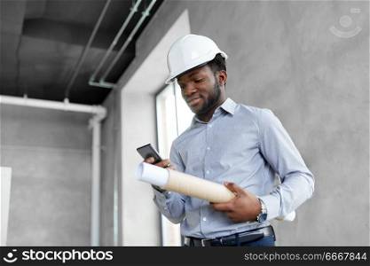 architecture, construction business and people concept - african american architect in helmet with blueprint and smartphone. architect in helmet with blueprint and smartphone. architect in helmet with blueprint and smartphone