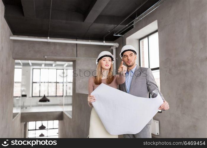 architecture, construction business and people concept - architects with blueprint and helmets at office pointing at something. architects with blueprint and helmets at office