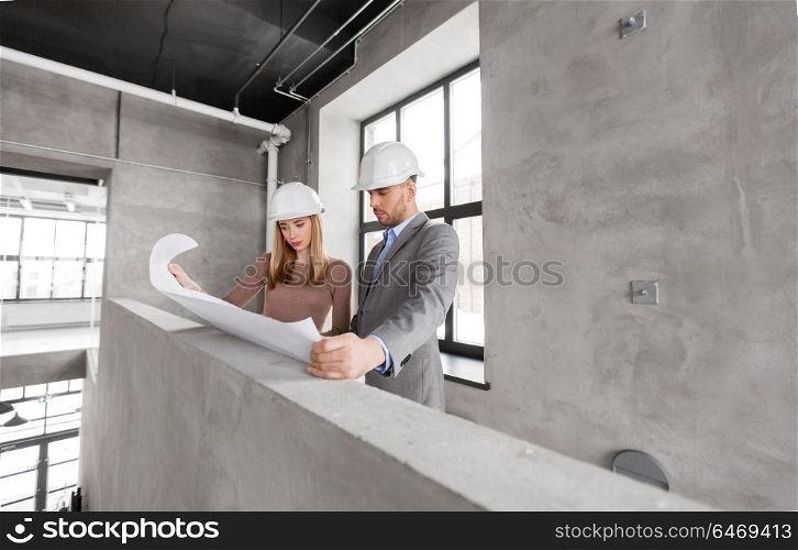 architecture, construction business and people concept - architects with blueprint and helmets at office. architects with blueprint and helmets at office