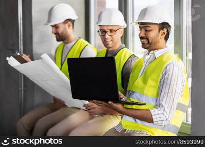 architecture, construction business and people concept - group of male architects in helmets with laptop, blueprint and clipboard working at office. male architects in helmets working at office