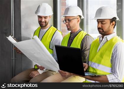 architecture, construction business and people concept - group of male architects in helmets with laptop, blueprint and clipboard working at office. male architects in helmets working at office