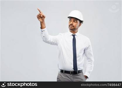 architecture, construction business and people concept - indian male architect in helmet pointing finger to something over grey background. indian male architect in helmet showing something
