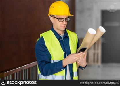 architecture, construction business and people concept - male architect in helmet with blueprint and smartphone at office. male architect with blueprint and smartphone