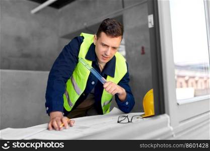 architecture, construction business and people concept - male architect with blueprint and ruler working on window sill at office. male architect with blueprint and ruler at office