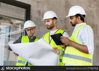 architecture, construction business and people concept - male architects in helmets with blueprint working in office building. architects with blueprint in office building