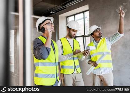 architecture, construction business and people concept - male architects in helmets with smartphone, blueprint and clipboard working at office building. male architects in helmets working at office