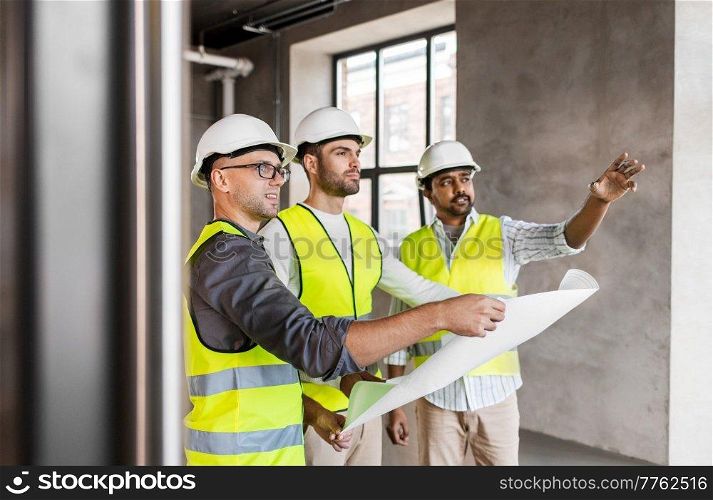 architecture, construction business and people concept - male architects in helmets with blueprint working at office building. architects in helmets with blueprint at office