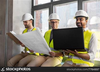 architecture, construction business and people concept - male architects in helmets with laptop, blueprint and clipboard working at office. male architects in helmets with laptop at office
